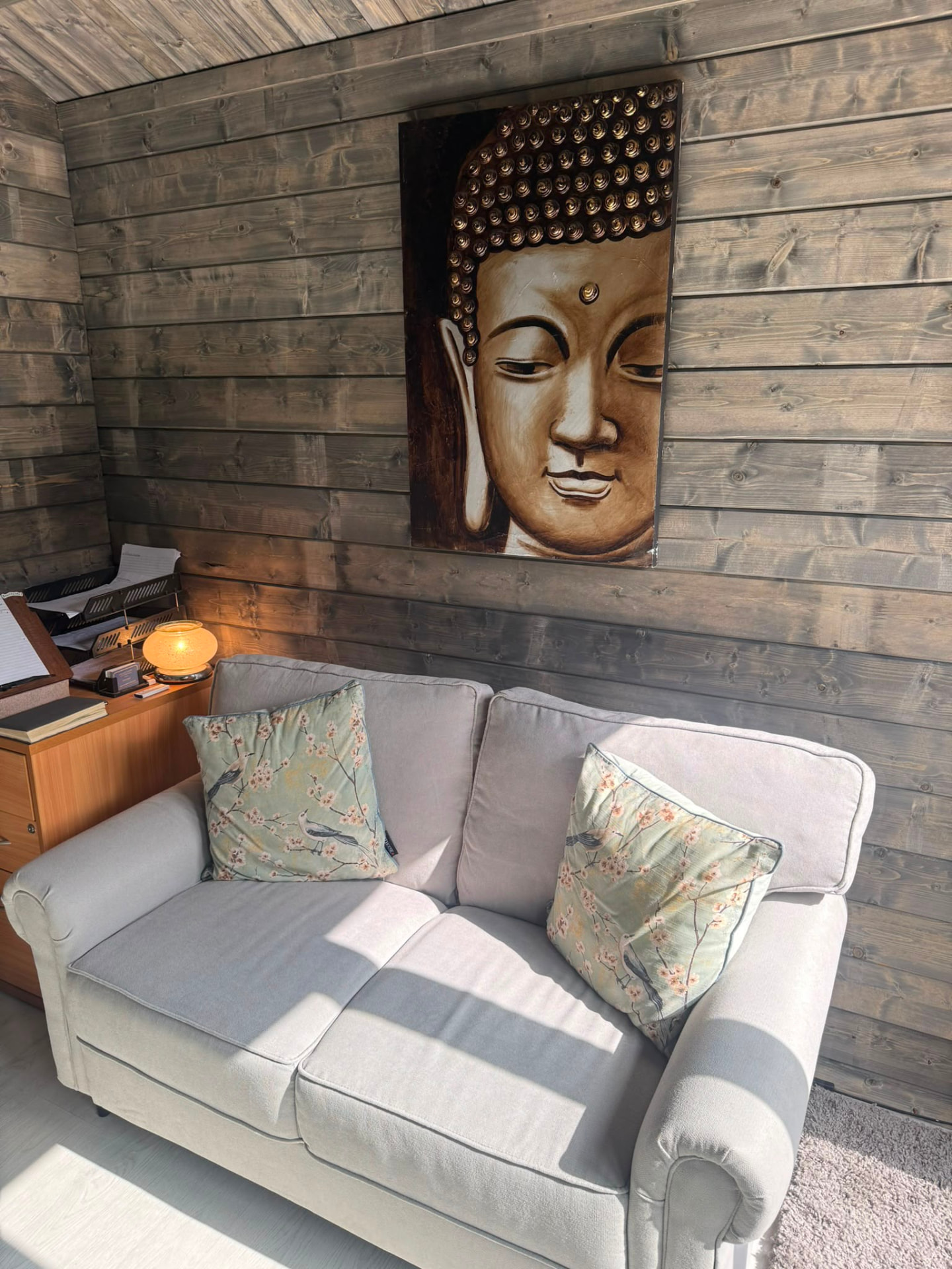 A comfortable grey sofa with floral cushions and Buddha wall art in the timber cabin